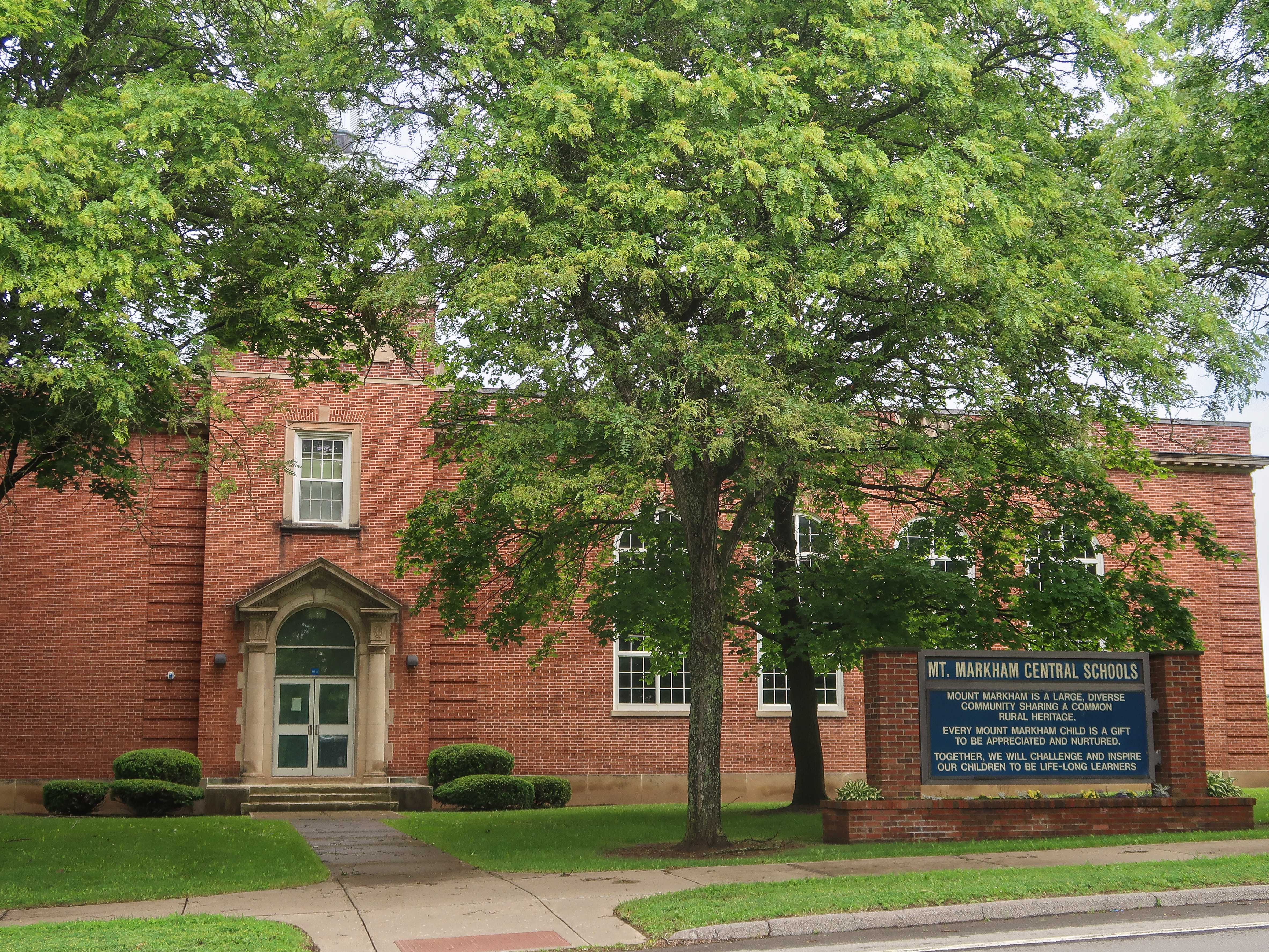 Brick building surrounded by leafy green trees.